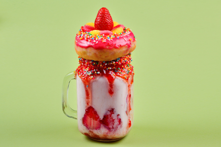 Freakshake. Extreme milkshake with strawberry, jelly sweets, donut on green background. の写真素材