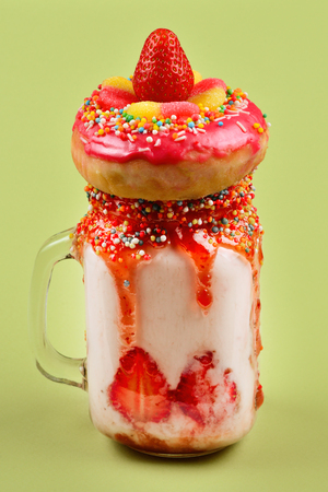 Freakshake. Extreme milkshake with strawberry, jelly sweets, donut on green background. の写真素材