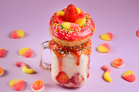 Freakshake. Extreme milkshake with strawberry, jelly sweets, donut on lilac background.の写真素材