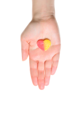 Woman hand with pale skin is holding jelly sweet heart isolated on white.の写真素材