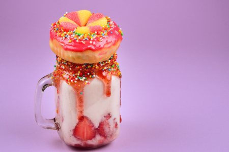 Freakshake. Extreme milkshake with strawberry, jelly sweets, donut on lilac background.の写真素材