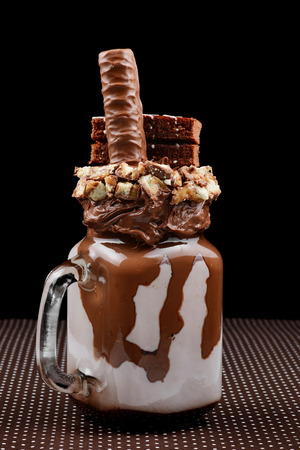 Chocolate extreme milkshake with brownie cake, chocolate paste and sweets. Crazy freakshake food trend. の写真素材