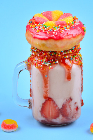 Freakshake. Extreme milkshake with strawberry, jelly sweets, donut on blue background. の写真素材