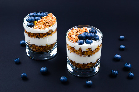 Homemade baked granola with yogurt and blueberries in a glass on a black background. Space for text or design.の写真素材