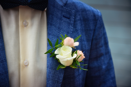 Groom in blue checkered suit with a white and pale pink rose boutonniere, close up.の写真素材