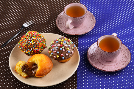 Baking with tea and chocolate on the table.  Two cups of tea with cupcakes and chocolate with a multicolored powder on the table.の写真素材