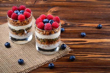 Healthy blueberry and raspberry parfait in a glass on a rustic brown wood background. Two portions. Space for text or design.の写真素材