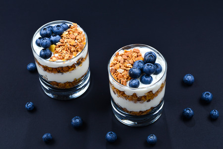 Homemade baked granola with yogurt and blueberries in a glass on a black background. Space for text or design.の写真素材