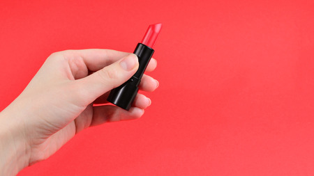Lipstick in woman hand isolated on red background.の写真素材
