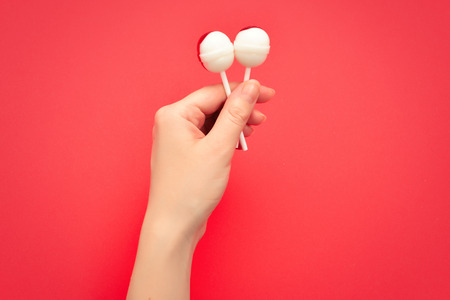 Lollipop in female hand on red background. Space for text or design.の写真素材