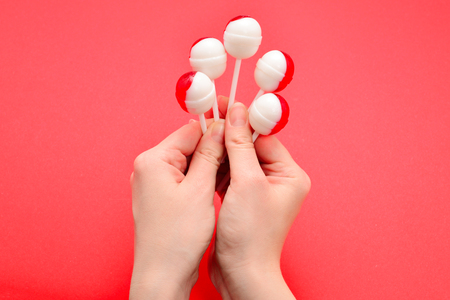 Lollipop in female hand on red background. Space for text or design.の写真素材