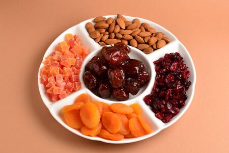 Mix of dried fruits and nuts on a white plate. Apricot, almond, raisin, dates fruit. On a brown background. Space for text or design.の写真素材