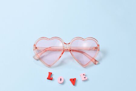 Pink sunglasses on a blue background with love text. Top view.の写真素材
