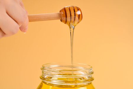 Dipper with honey in woman hand on orange background. Space for text or design.の写真素材