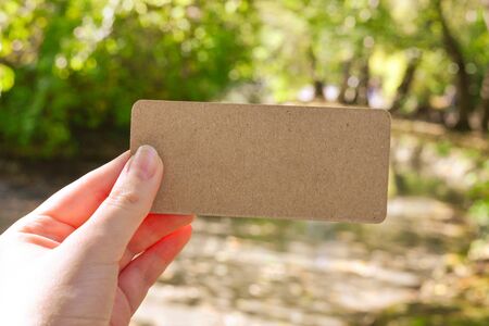 Hand holding empty card in park in sunny rays.  Background. Copy space.の写真素材
