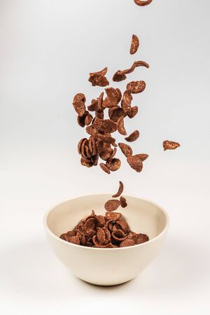 Chocolate corn flakes falling to the white bowl isolated on white. Motion. Copyspace.の写真素材