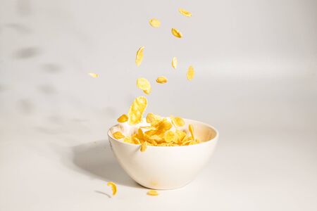 Corn flakes falling to the white bowl. Motion. Copyspace. Isolated on white.