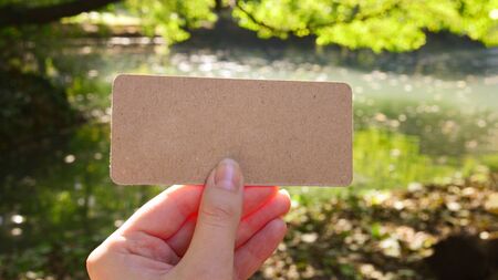 Hand holding empty card in park in sunny rays.  Background. Copy space.の写真素材