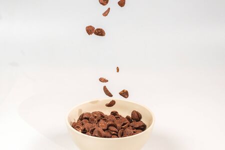 Chocolate corn flakes falling to the white bowl isolated on white. Motion. Copyspace.の写真素材