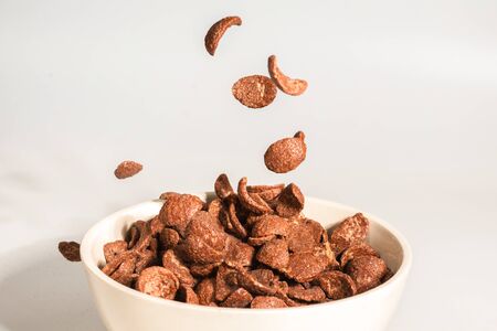 Chocolate corn flakes falling to the white bowl isolated on white. Motion. Copyspace.の写真素材