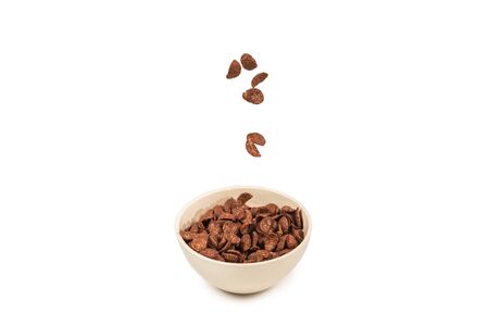 Chocolate corn flakes falling to the white bowl isolated on white. Motion. Copyspace.の写真素材