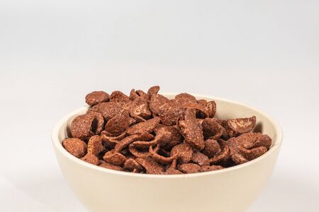 Chocolate corn flakes falling to the white bowl isolated on white. Motion. Copyspace.