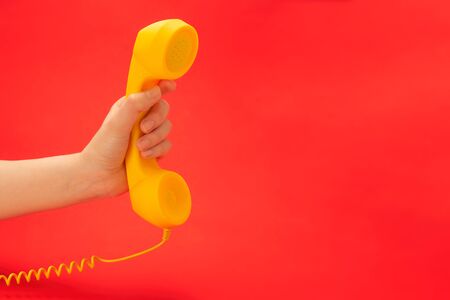 Yellow handset on a red background in woman hand. Copy space.の写真素材