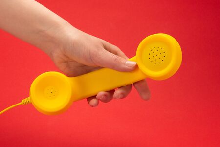Yellow handset on a red background in woman hand. Copy space.の写真素材