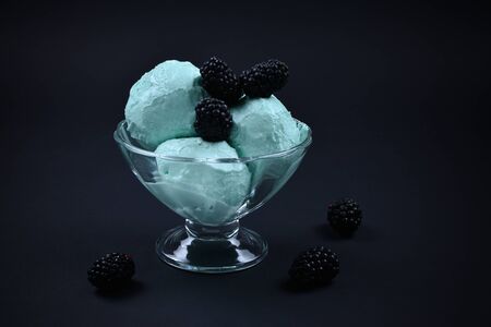 Blue ice cream in cup with berry on black background.の写真素材