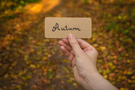 Autumn text on a card.  Girl holding card in autumn park in sunny rays.の写真素材