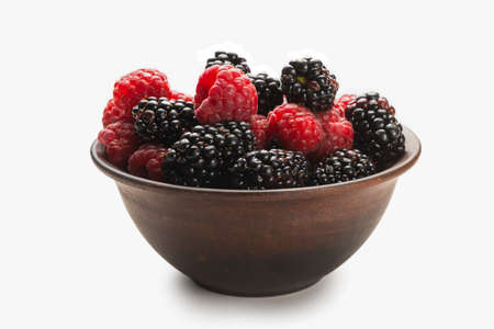 Raspberry, blackberry and mint leaf in ceramic brown bowl isolated on white background.