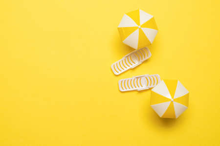 Two sun loungers and a red umbrella on a yellow background. Copy space.