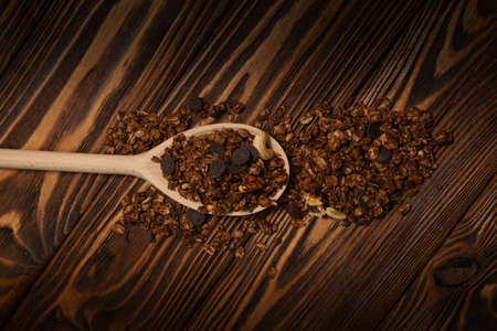 Chocolate granola cereal with nuts in a wooden spoon. On a wooden background.の写真素材