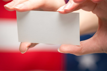 Empty card in woman hand. Copy space. American flag background.の写真素材