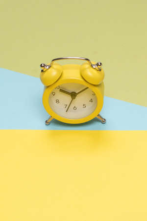 Yellow alarm clock on a yellow, blue and green background. Copy space. Time concept.