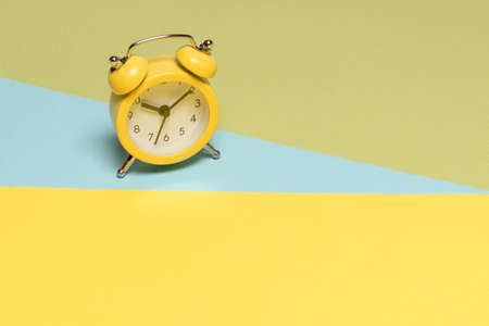 Yellow alarm clock on a yellow, blue and green background. Copy space. Time concept.の写真素材