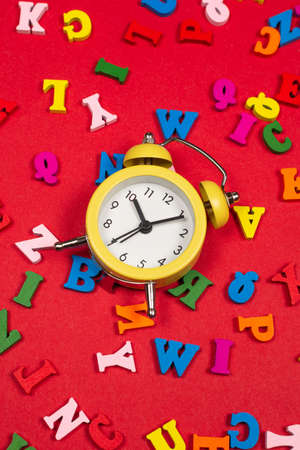 Random colorful alphabet and yellow alarm clock on a red background, colorful letters. Time to school. Study time. Education time.の写真素材
