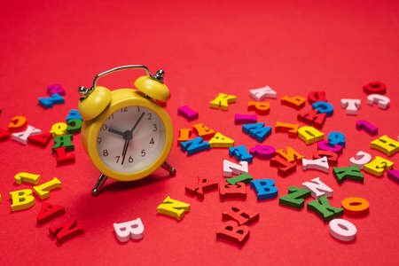 Random colorful alphabet and yellow alarm clock on a red background, colorful letters. Time to school. Study time. Education time.の写真素材