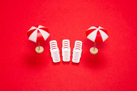 Two sun loungers and red umbrellas on a red background. Copy space.