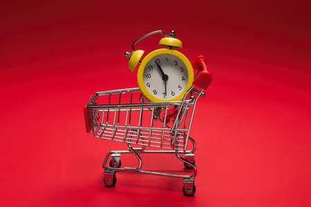 Shopping time. Yellow alarm clock in shopping basket on a red background. Copy space.の写真素材