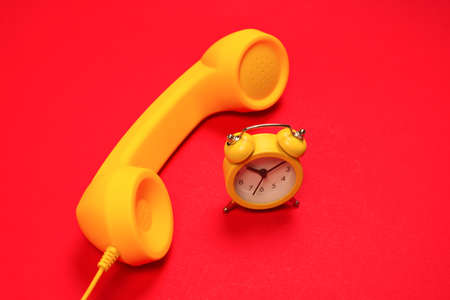 Time to call. Yellow handset and alarm clock on a red background. Copy space.の写真素材