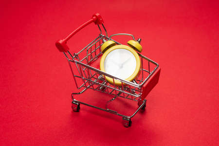 Shopping time. Yellow alarm clock in shopping basket on a red background. Copy space.の写真素材