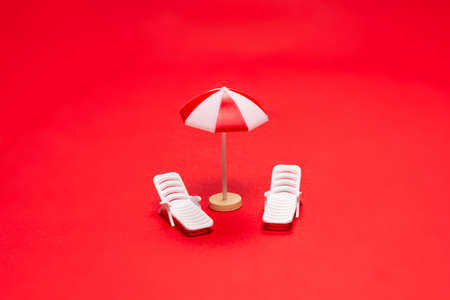 Two sun loungers and red umbrellas on a red background. Copy space.の写真素材