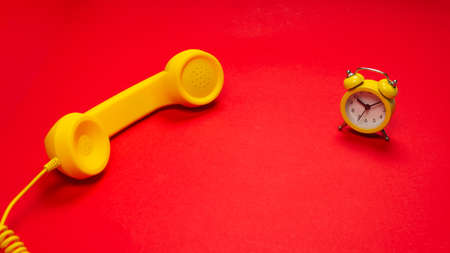 Time to call. Yellow handset and alarm clock on a red background. Copy space.の写真素材