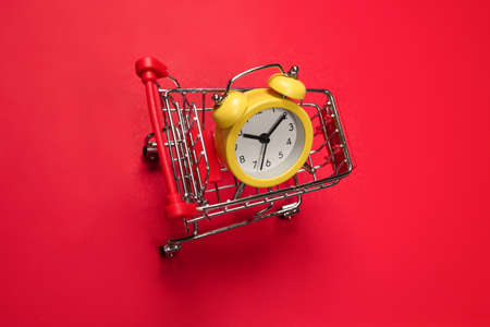 Shopping time. Yellow alarm clock in shopping basket on a red background. Copy space.の写真素材