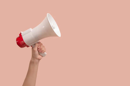 Megaphone in woman hands on a pink background. Copy space.