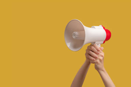 Megaphone in woman hands on a yellow background. Copy space.の写真素材