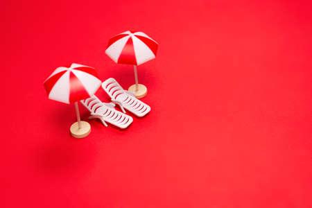 Two sun loungers and red umbrellas on a red background. Copy space.の写真素材
