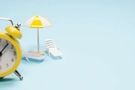 Time to travel. Sun lounger, umbrella and alarm clock on a blue background.の写真素材