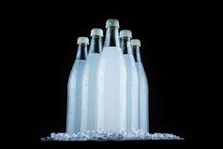 A white bottle with a soda drink on ice on a black background.